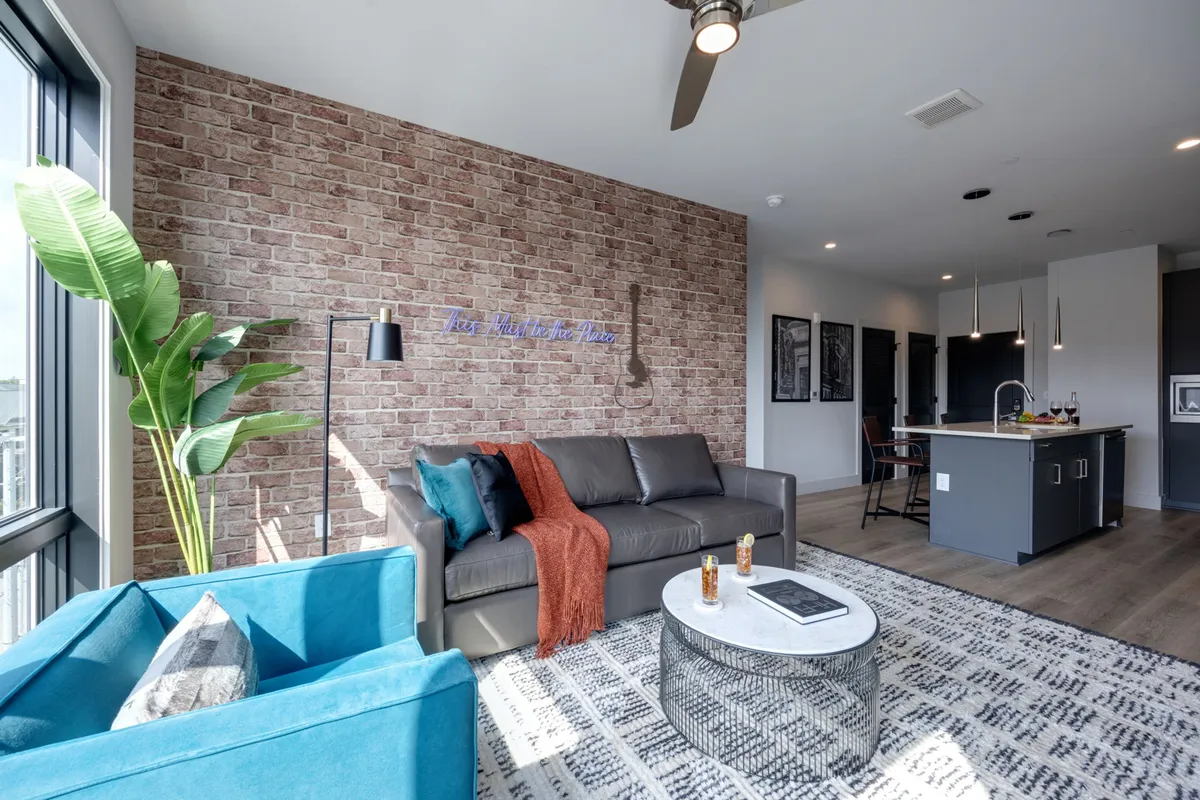The image showcases a cozy, inviting living room with an exposed brick wall, a plush sofa adorned with throw pillows, a vibrant armchair, and a stylish coffee table. The setup encourages relaxation and social gatherings, making it perfect for group stays or family get-togethers.