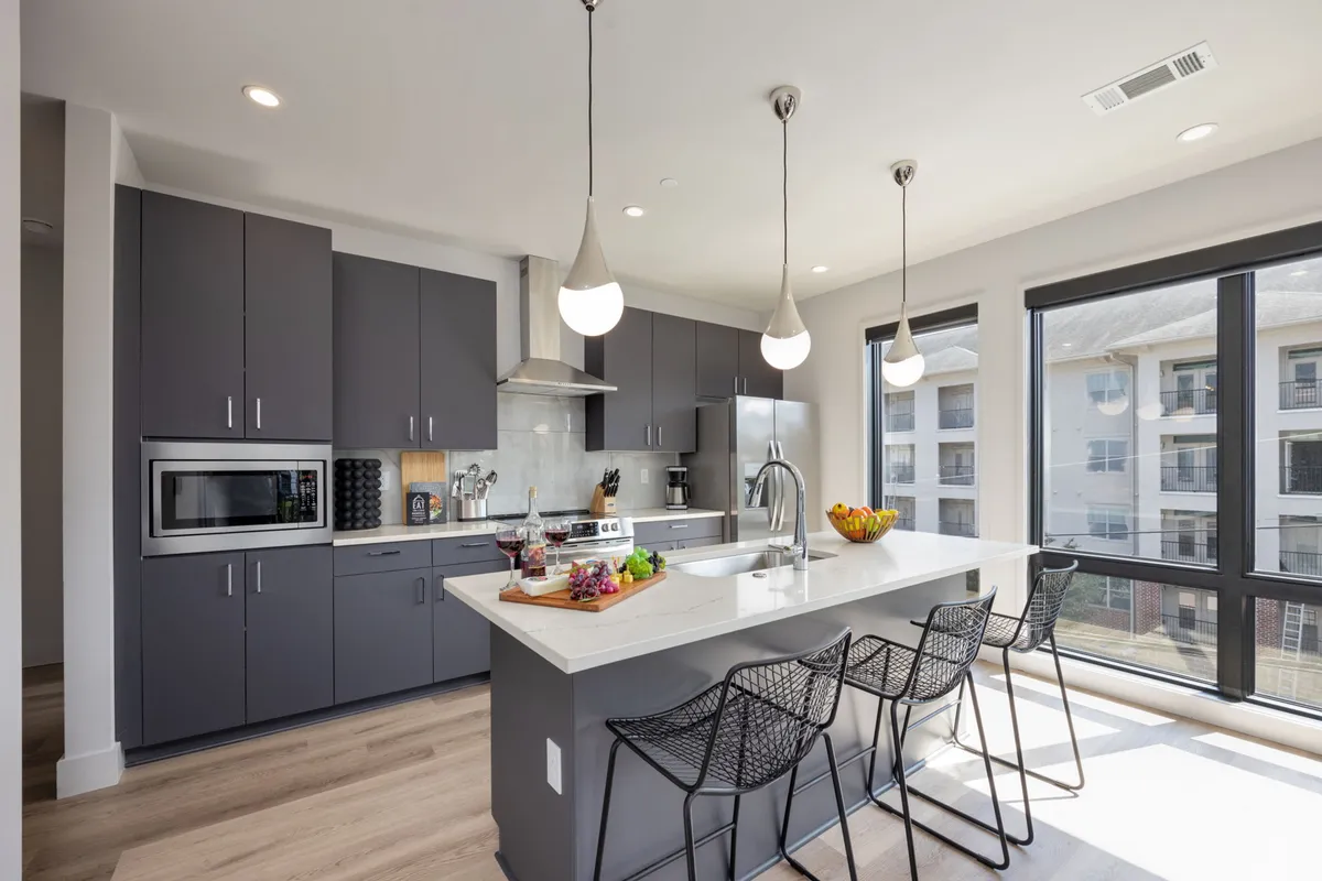 A contemporary kitchen with a prominent island, hanging light fixtures, and modern appliances, including a clear window view. The island is ideal for cooking, entertaining, and sharing meals, and the warm lighting creates an inviting atmosphere.
