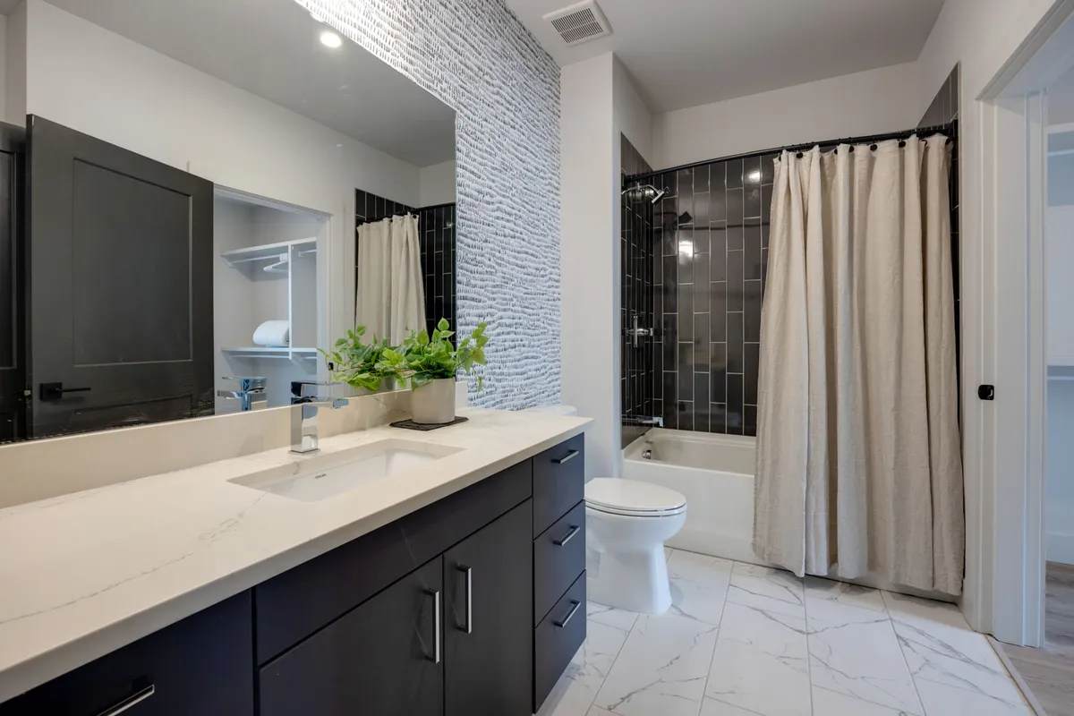 A contemporary bathroom with a sleek vanity and sink, black tiled walk-in shower, textured accent wall, and a bathtub offers both luxury and versatility. The calm palette and modern fixtures evoke a tranquil, spa-like experience.