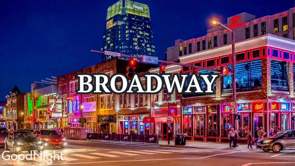 A lively nighttime street view featuring glowing neon signs, bustling crowds, and the vibrant atmosphere typical of Nashville’s Broadway area. Skyscrapers and the energetic movement of people hint at the city’s renowned nightlife and live music culture.