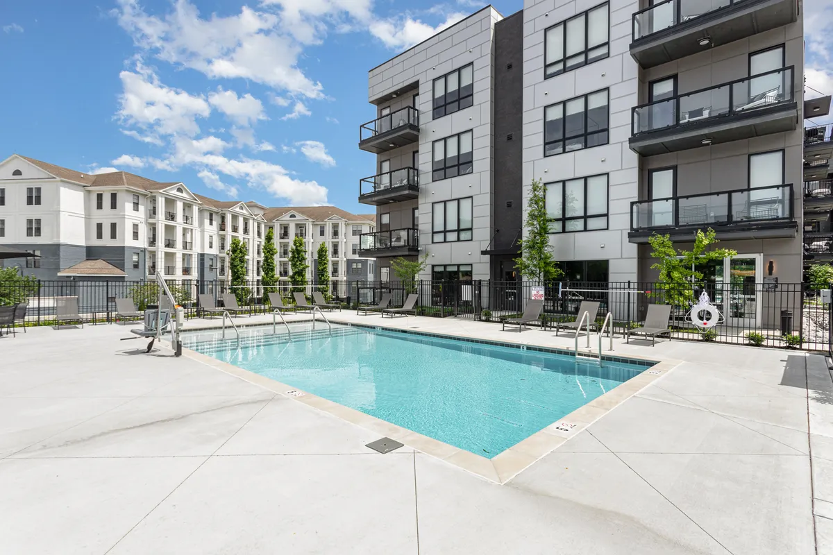 A resort-style swimming pool surrounded by apartment balconies and communal outdoor spaces. The setting is relaxed, with lounge areas inviting both socializing and late-night swims under the city lights.