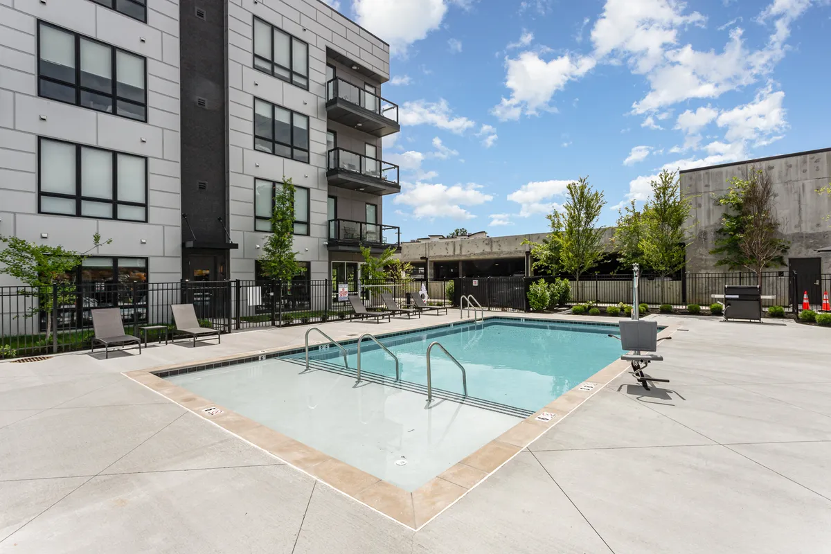 An inviting exterior view of the swimming pool surrounded by landscaped greenery, balconies, and lounge chairs. The setting is ideal for summer barbecues, pool parties, or quiet afternoons, with clear views of the communal outdoor space.