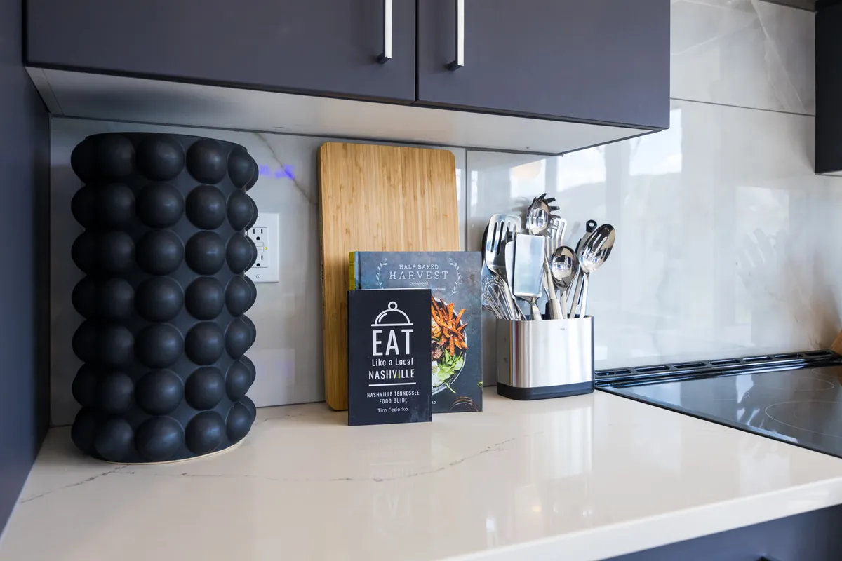 A stylish kitchen countertop with a wooden cutting board, a decorative black vase, utensils, and a cookbook titled 'EAT Like a Local NASHVILLE.' The setting feels contemporary yet welcoming, suggesting culinary adventures at home.